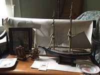 Overall view of lot showing model ship, two Syroco bookends, framed painting, ceramic candlestick and two plates on wooden surface