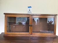 Front view of the oak display case showing two glazed glass doors with brass pulls, placed on a wooden surface.