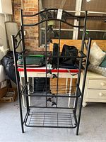 Full front view showing the entire black metal baker's rack with three shelves and standing legs
