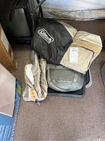 Photo showing two folded Coleman inflatable air mattresses and a folded Coleman Arctic sleeping bag stored in a bin on carpeted floor.