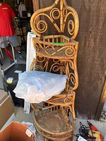 Full view of 3-tier rattan/bamboo corner shelf unit showing structure, wear, and bag of silk flowers on top.