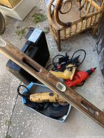Overview of power drills, grinder, blades, and one wooden bubble level on the ground near wicker furniture.