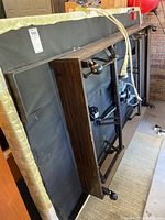 Underside of Flex-A-Bed adjustable bed frame showing wooden panel, metal supports, wheels, and beige box spring fabric.