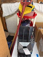 Photo showing red mop handles, plastic wheeled storage cart, black plastic file and magazine organizers, and U.S. Open Golf Tour collector caps.