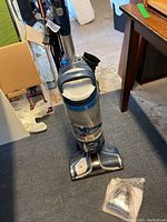 Hoover React upright vacuum showing the full unit and an attachment on the floor.