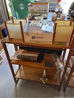 Wooden fold-up shelf unit holding incense burners, new light bulbs, incense sticks, small ceramic mugs, and other small items. Shelf has canvas sides and a wooden frame.