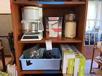 Shelf with Mr. Coffee Auto-Drip Coffeemaker, Rival Electric Can Opener box, Sunbeam Oskar chopper, blue plastic tub with various tools, and two Pro Smart Mandolin slicers