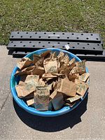 Multiple brown paper mystery bags in a blue kiddie pool with black plastic garden board frames behind.