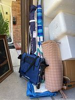 Blue Nautica beach umbrellas with protective covers and handles, along with cotton-covered roll-out cot cushion and other items stacked outside.