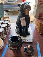 Full view of the black ceramic Florida black panther statue with open mouth, showing the statue seated on a table next to the black ceramic vase without its lid.