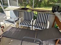 Three white PVC chairs with blue and white striped cushions arranged side by side on a covered patio area with visible signs of slight weathering and fading on cushions.