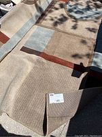 Full view of the Mohawk Home Holton Sutton beige patterned area rug laid out on floor, showing pattern and colors including beige, brown, light blue and rust accents. Corner lifted to see edge.