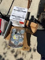 Top view showing Zojirushi rice cooker box and pack of various glass canning jars in open cardboard box on ground outdoors.