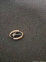 Oval shaped 14KT gold service pin with black enamel and clear stones showing the front side with the Lockheed logo.