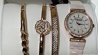 Anne Klein watch and three matching bracelets displayed on a white cushion inside white presentation box.