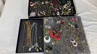 Overview of the collection showing trays with assorted vintage earrings and necklaces displayed on black backgrounds