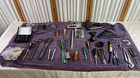 Full overview of all assorted hand tools laid out on a purple cloth, showing screwdrivers, wrenches, clamps, measuring tools, and pliers.