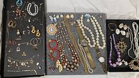 Full overview of collection spread on flat surface showing earrings, pins, necklaces, and watches.