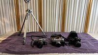 Three vintage 35mm film cameras (Minolta SRT-102, Canon Canonet S, Minolta Maxxum 3xi) displayed on a purple cloth.