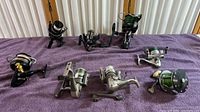 Overview of eight fishing reels on purple towel showing varied sizes and brands including Penn, NGT, and Shimano