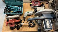 Ryobi miter saw visible with corded drill in case and Makita power planers on table.