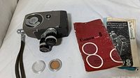 Full view of the vintage Canon Eight camera with attached lens, instruction booklet, lens cap, and circular lens accessory on a white fabric surface.