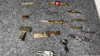 Photo showing all 13 vintage gold and silver tone tie clips spread out on gray felt background.