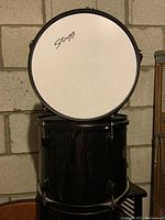 Photo showing two black Stagg drums stacked, with white drum head visible on top drum, slight surface dust and basement storage setting