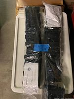 Two unopened black Volkswagen CarGo Management Systems in plastic bags with labels and instruction sheets visible, resting on a white bin.