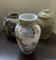 Three vases arranged together on table: central tallest floral and bird patterned vase, two rounder containers behind.