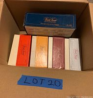 Top-down view of 5 boxed Trivial Pursuit board games in various colored boxes inside a plain cardboard box.
