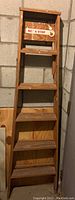 Full view of the 6-foot wooden ladder showing five steps and a top platform, with a caution sign reading 'NO A STEP' on the uppermost step.
