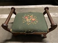 Top view of antique footstool showing green embroidered fabric with floral pattern and visible damage to upholstery.