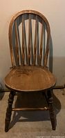 Front view of the antique wooden chair showing the rounded back, contoured seat, and turned legs.