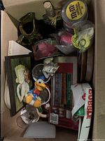Top-down view of box containing assorted vintage collectible items such as ceramic pitcher, candle holders, cracker dish, shot glasses, mugs, and figurines.