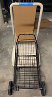 Photo of the grocery cart showing its black metal mesh basket, handle, and two wheels from an overhead angle.