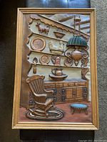 Front view of the 3D relief framed artwork showing a rustic kitchen scene with a chair, cabinet, shelves with dishes, and a hanging lamp.