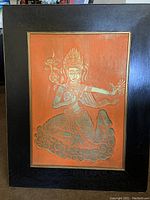 View of framed gold relief print artwork depicting a traditional Thai figure, emphasizing the details of the figure and frame.