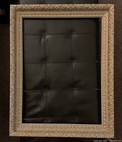 Front view of vintage white and gold ornate picture frame on dark surface, showing detailed carved patterns and condition.