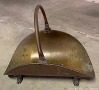 Side view of curved brass firewood holder showing overall shape and arched handle.
