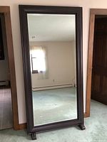 Full view of front of mirror standing upright in room showing dark wood frame and two feet.