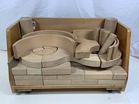 Front view of wooden rolling cubby with natural wood blocks arranged inside, showing curved and cylindrical blocks on top and rectangular blocks underneath.