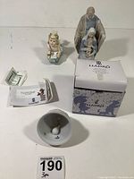Three figurines displayed with LLadro box and papers, bell turned upside down showing LLadro logo inside