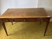 Front view of the desk showing three drawers with round metal knobs and tapered legs.