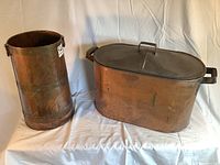 Photo of the tall cylindrical copper bucket and the large rectangular copper tub with lid and handles displayed side-by-side.