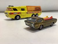 Side angle of the Hot Wheels Deora and Matchbox K-7 transporter showing color and surfboards