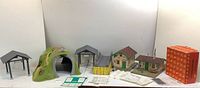 Photo of three large model structures, including a tunnel with hillside, two picnic or waiting shelters, multiple instruction sheets, and a boxed item.