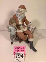Front view of porcelain figurine showing Santa Claus seated on stool with boy holding toy