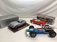 Full group shot showing the silver Burago Mercedes 300 SL model on wooden base with box, the red Deluxe Open Sedan tin toy with original box, and the blue Gama race car.