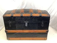 Closed view of the black dome top trunk with wood slats and metal hardware, showing latches and central lock